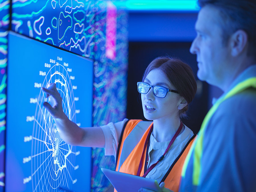 Female geologist with colleague studying graphical display of oil and gas bearing rock on screens